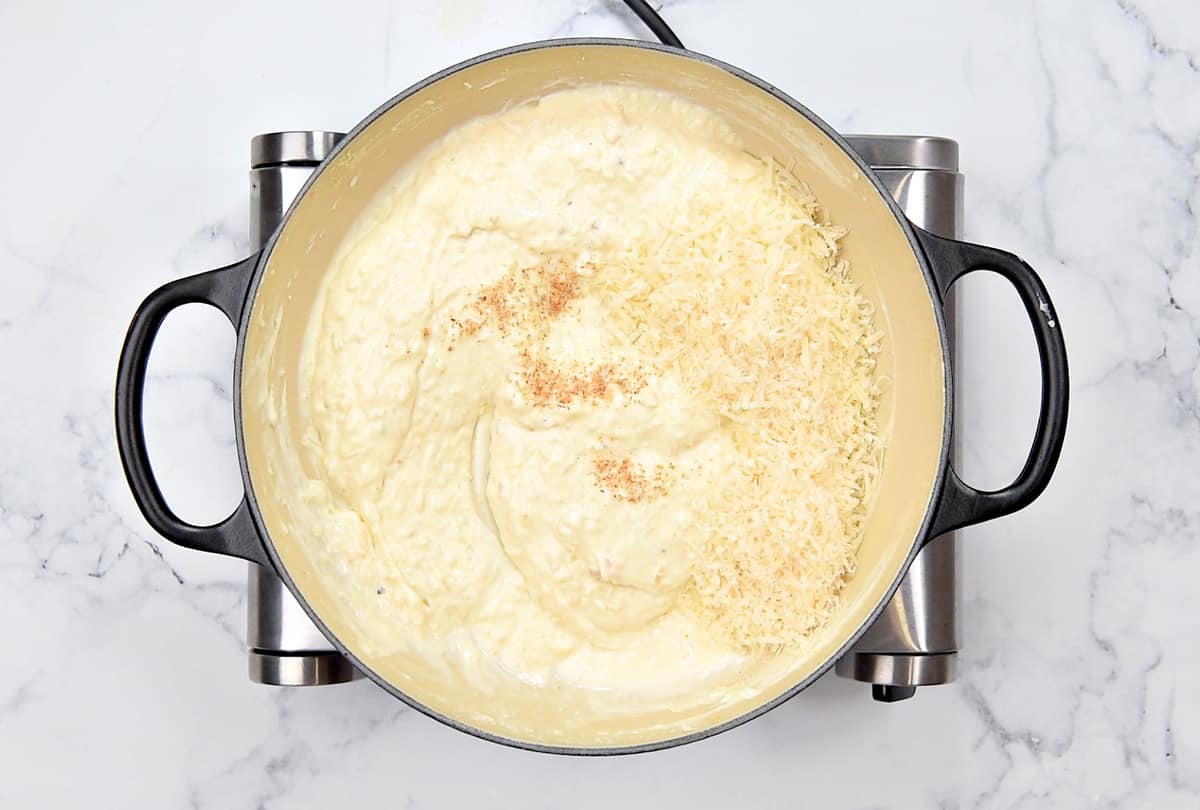 Adding nutmeg and cheese to the dish.