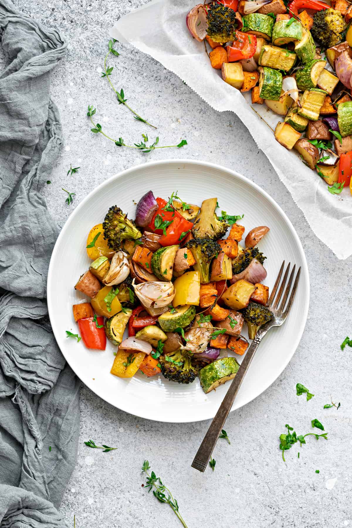 White plate with hearty roasted vegetables and a fork on a gray table.