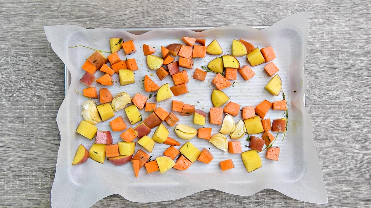 Diced sweet potatoes and red potatoes on a parchment paper lined baking sheet.