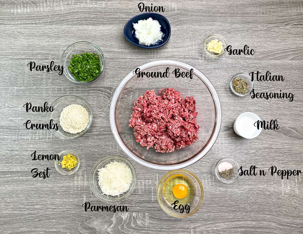 Recipe ingredients: Ground beef, seasonings, milk, egg, grated parmesan, lemon zest, panko, fresh parsley in glass bowl.