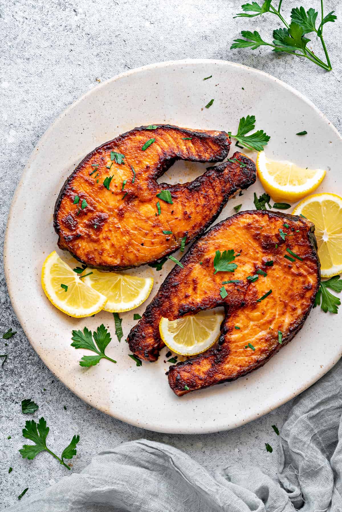 Top down plate with two air fryer salmon steaks with slices of lemon and parsley.