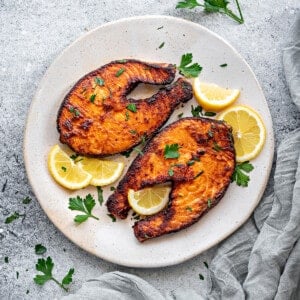 Top down plate with two air fryer salmon steaks with slices of lemon and parsley.