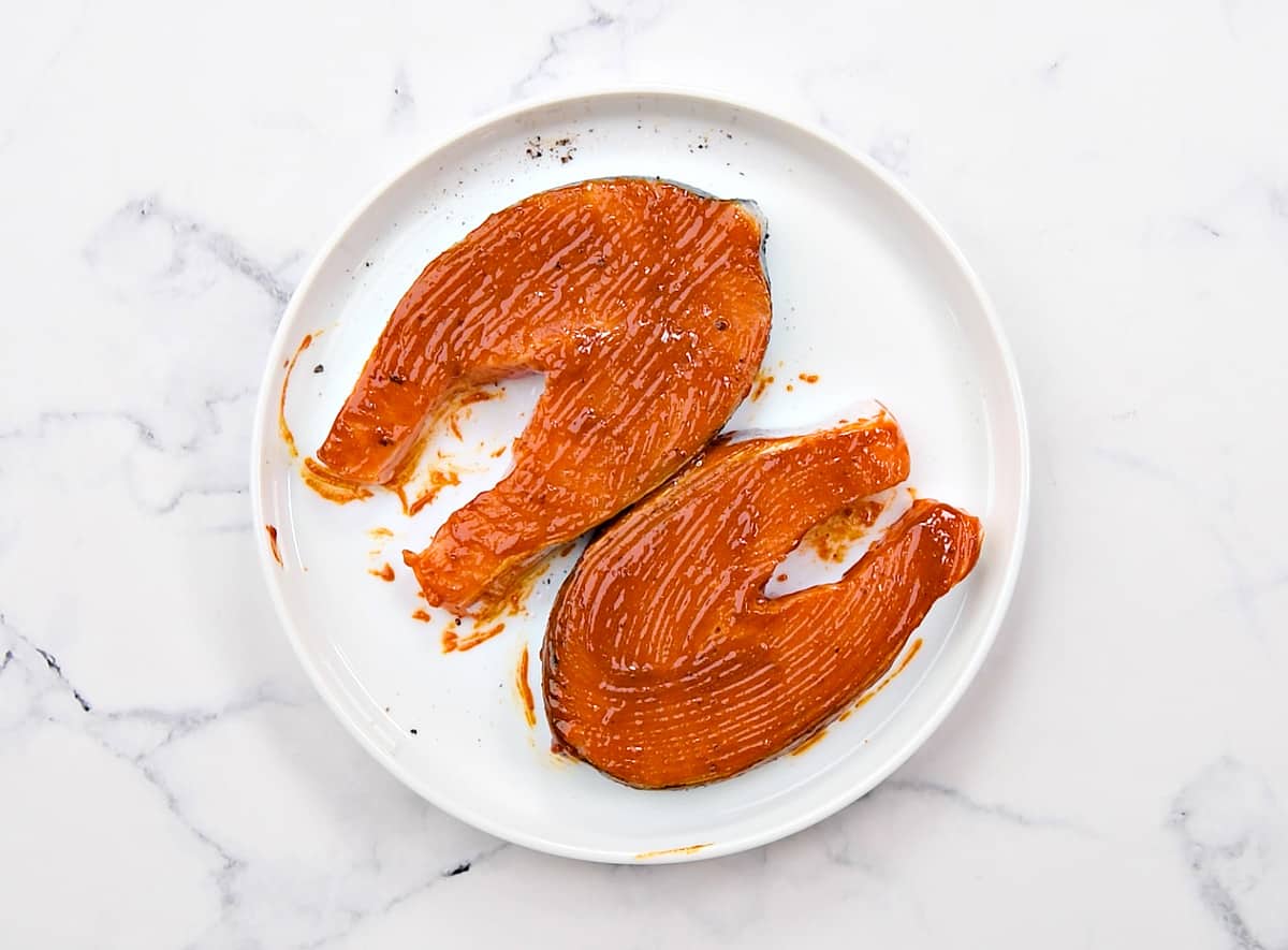 Two salmon steaks on a white plate brushed with marinade.