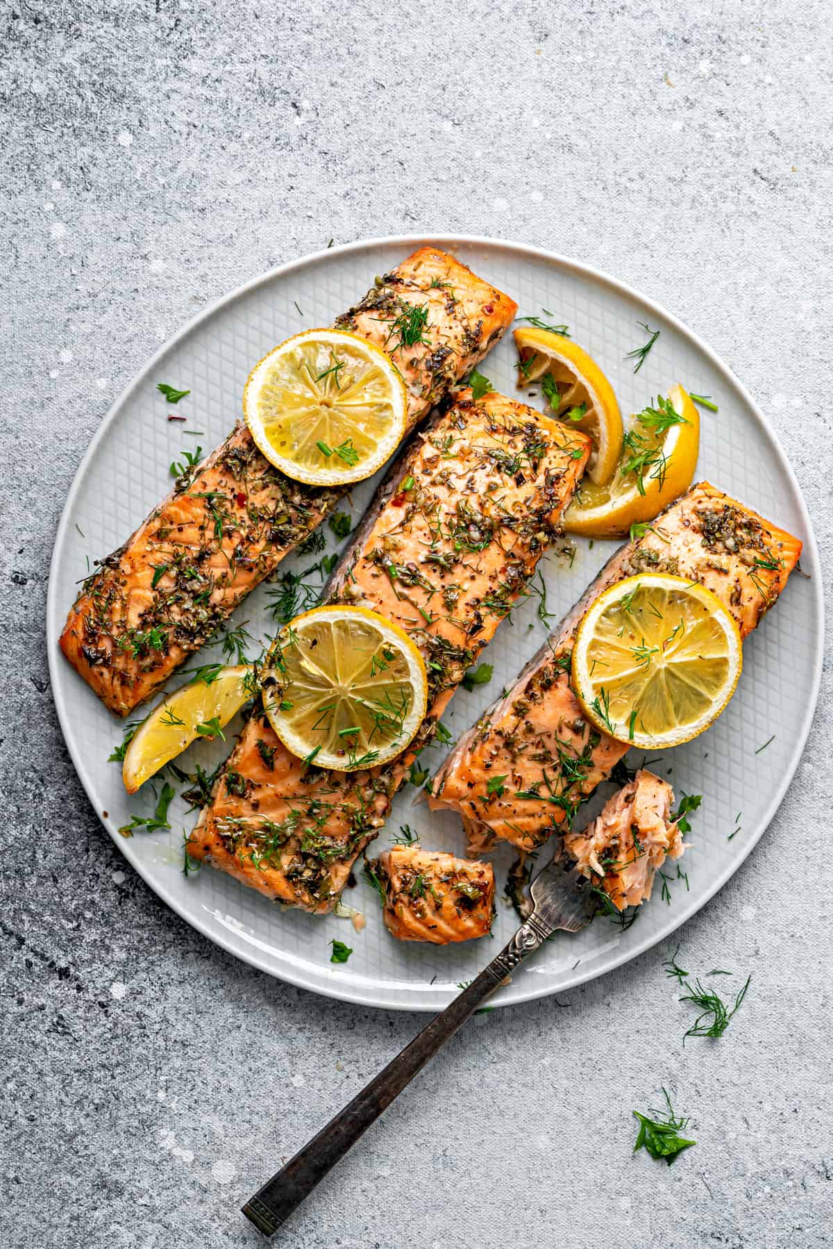 Fork taking bite from finished baked salmon recipe dish. 3 portions on a plate.