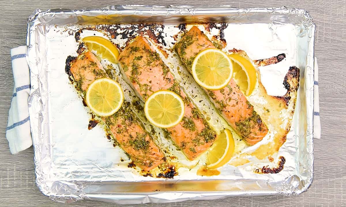 Baked salmon with herbs and lemon slices on a foil lined baking sheet.