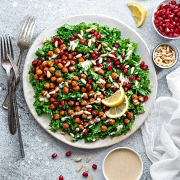 Overhead shot of vegan, gluten-free kale salad on a plate with ramekin of tahini sauce on the side.