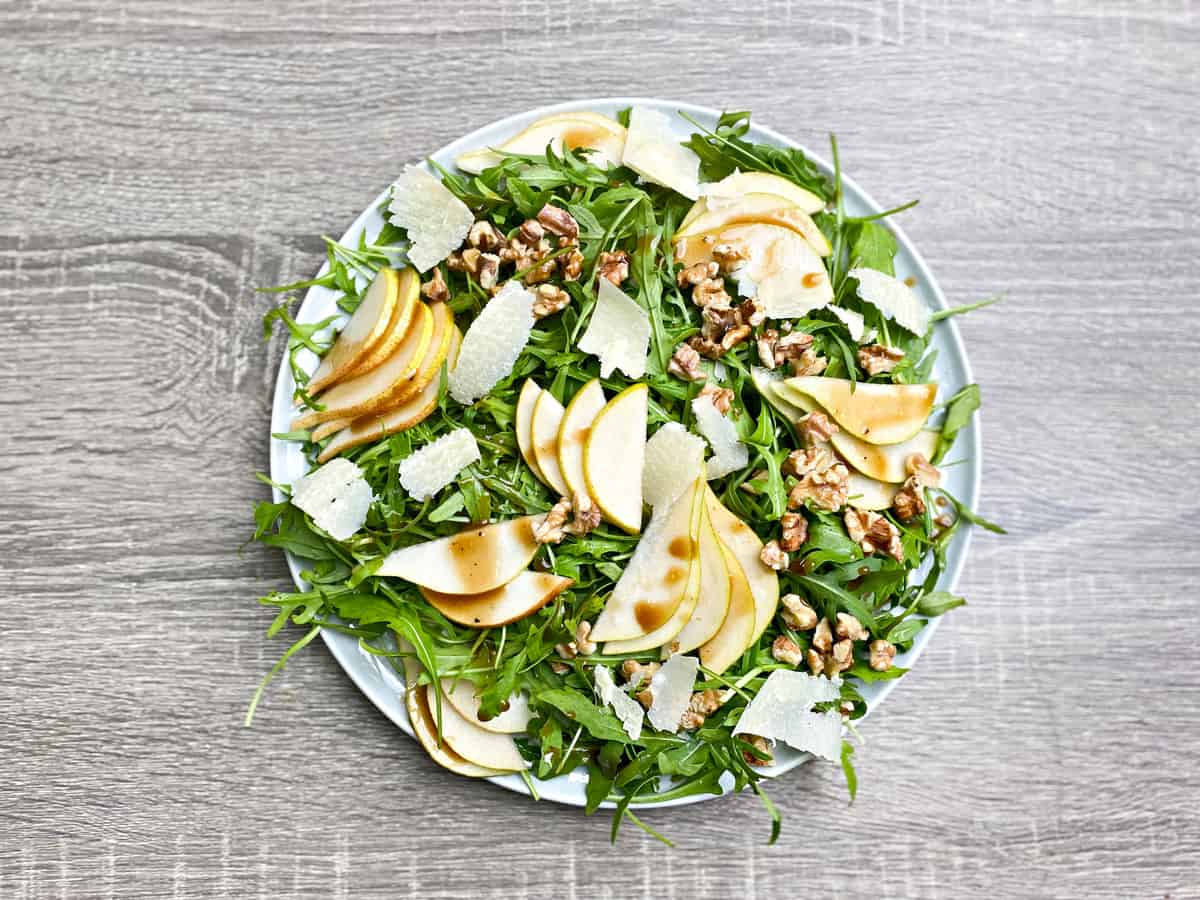 Top down large plate of pear salad with rocket, shaved parmesan cheese, chopped walnuts, and a balsamic vinaigrette.