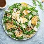 Top down large plate of rocket, walnuts and pear salad drizzled with balsamic vinaigrette.