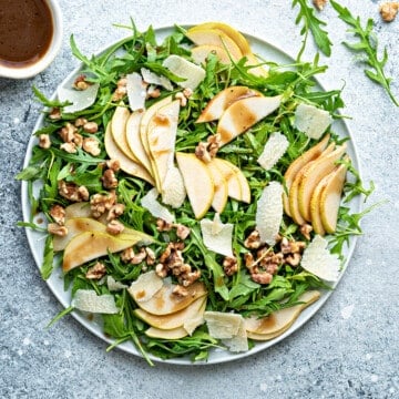 Top down large plate of rocket, walnuts and pear salad drizzled with balsamic vinaigrette.