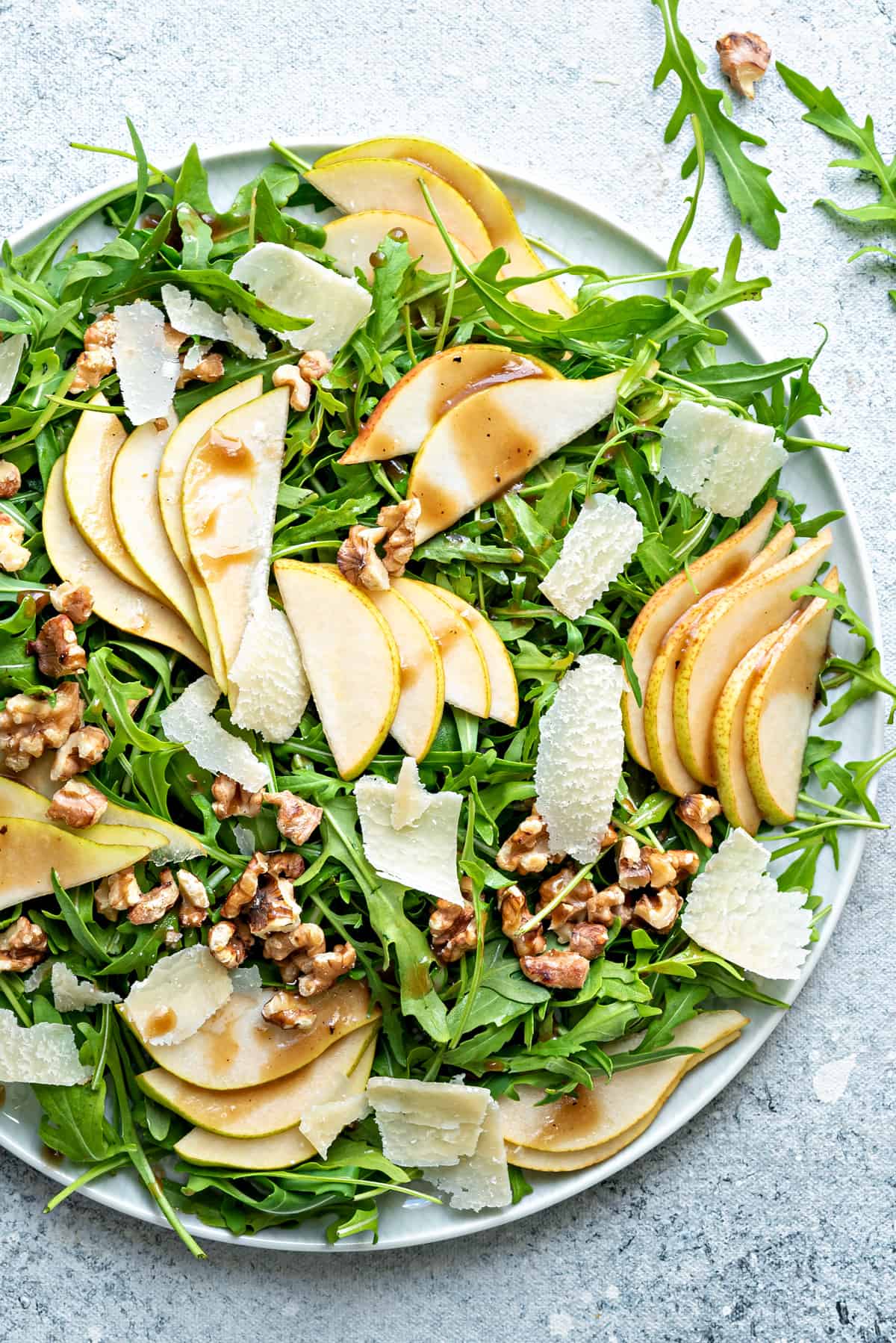 Top down close-up of large plate of rocket, walnuts and pear salad drizzled with balsamic vinaigrette. 
