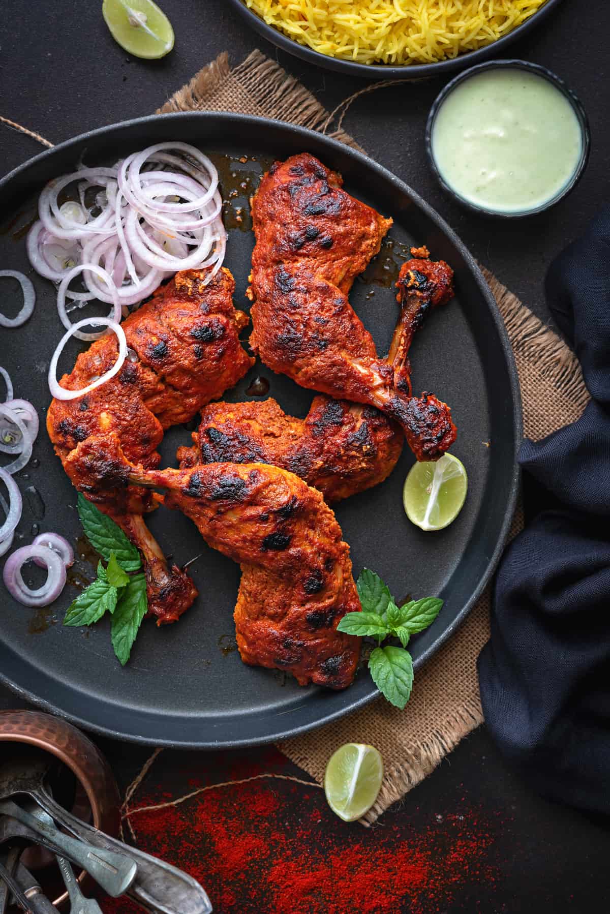 Tandoori chicken masala on round black tray, saffron rice, onion rings, lemon and chutney on side.