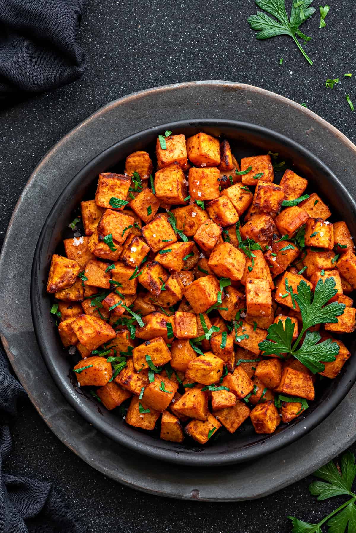 Top down view black plate with air fryer sweet potato cubes garnished with fresh parsley.