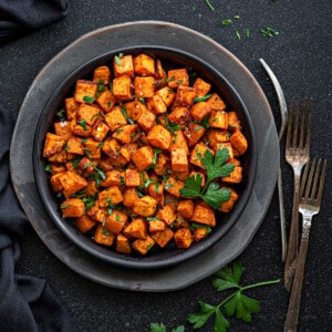 Black plate with air fryer sweet potatoes garnished with fresh parsley.