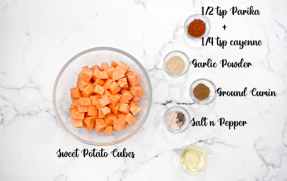 Recipe ingredients in glass bowls: Orange potatoes, paprika, garlic powder, ground cumin, salt, pepper, and oil.