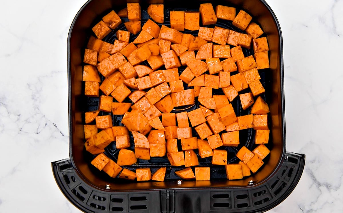 Sweet potato cubes spread evenly in the basket of the air fryer.
