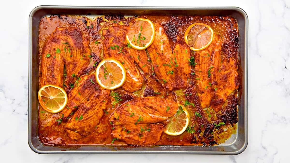 Sheet pan with baked tilapia in chili lemon marinade with fresh lemon slices ready to serve.