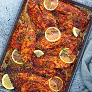 Top down view plate with chili lemon baked tilapia fillets with fresh lemon slices.