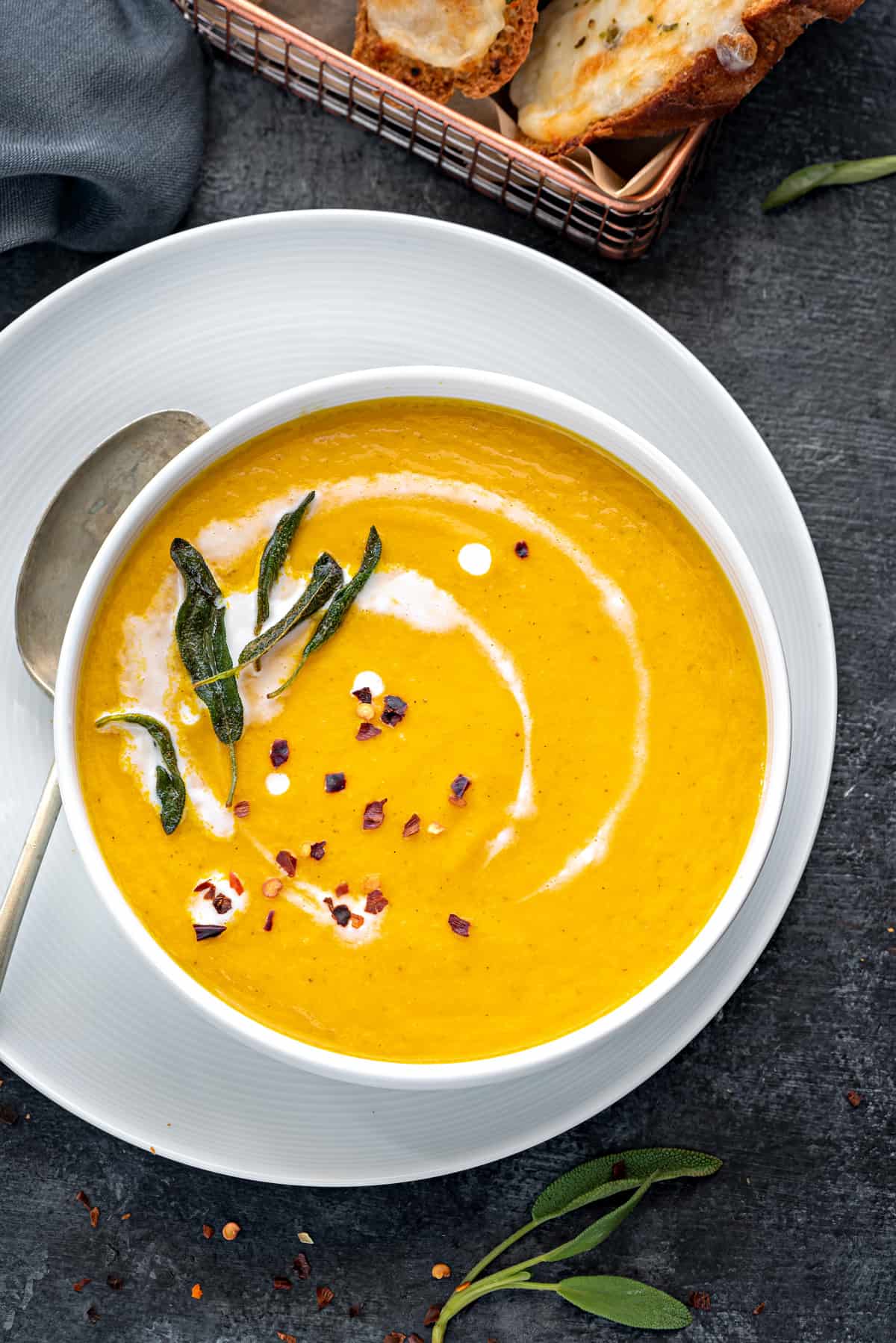 close-up of white bowl with roasted pumpkin soup, topped with fried sage and a spoon.