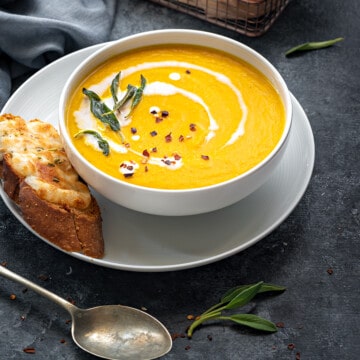 Roasted pumpkin soup served in white bowl with cheese toast on side.