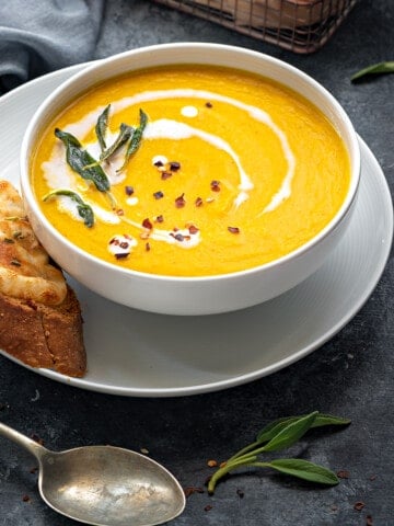 Roasted pumpkin soup served in white bowl with cheese toast on side.