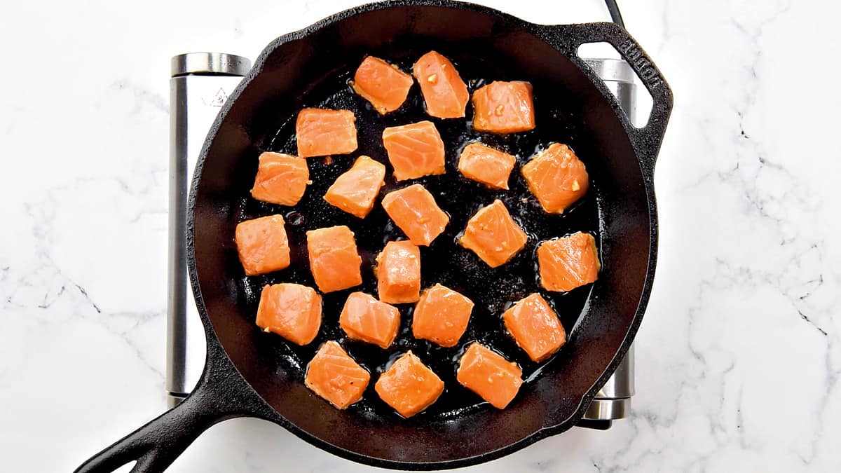 1-inch cubes of marinated salmon searing in a skillet.
