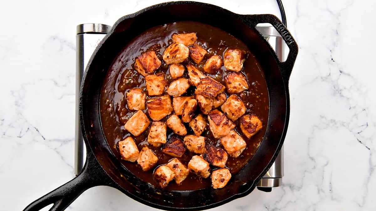 Adding the cooked salmon cubes back to the Asian sauce in the cast iron.
