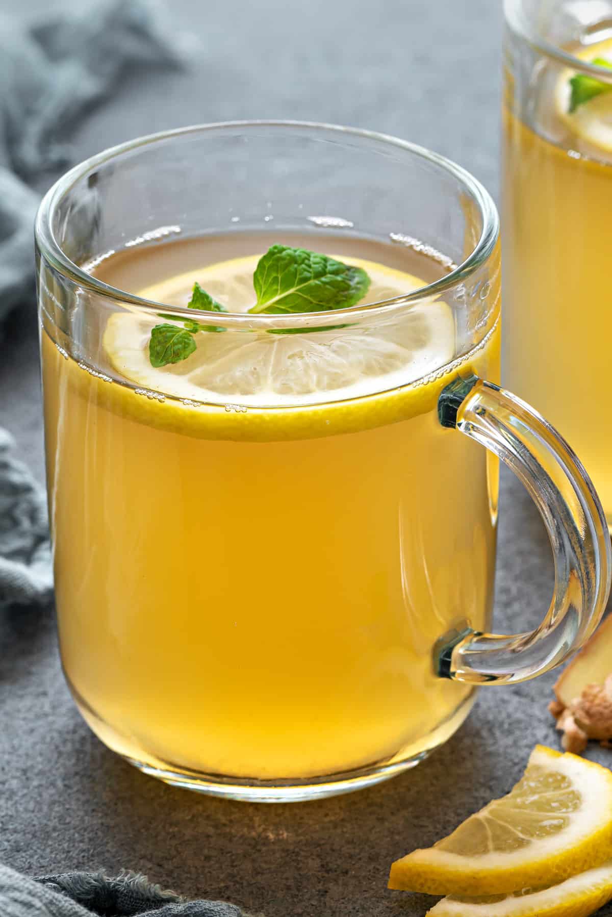 Close-up of a mug with ginger lemon tea garnished with lemon slices and fresh mint leaves.