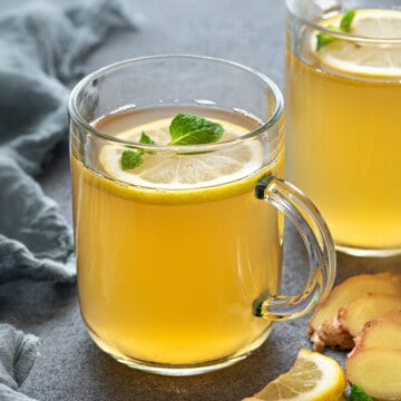 Two glass mugs of lemon ginger tea, garnished with lemon slices and fresh mint.