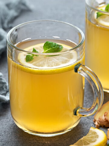 Two glass mugs of lemon ginger tea, garnished with lemon slices and fresh mint.