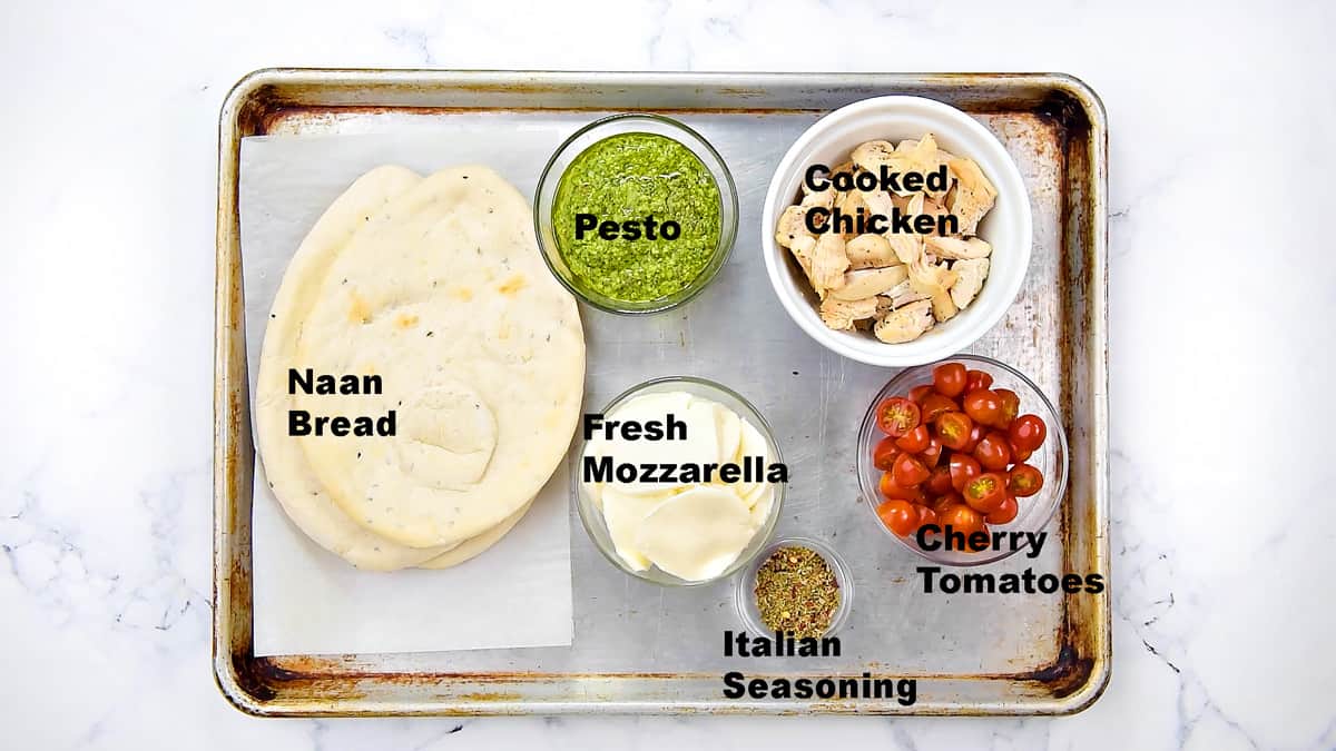 Recipe ingredients: naan breads, pesto, cooked chopped chicken, cherry tomatoes, fresh mozzarella slices, and Italian seasoning.