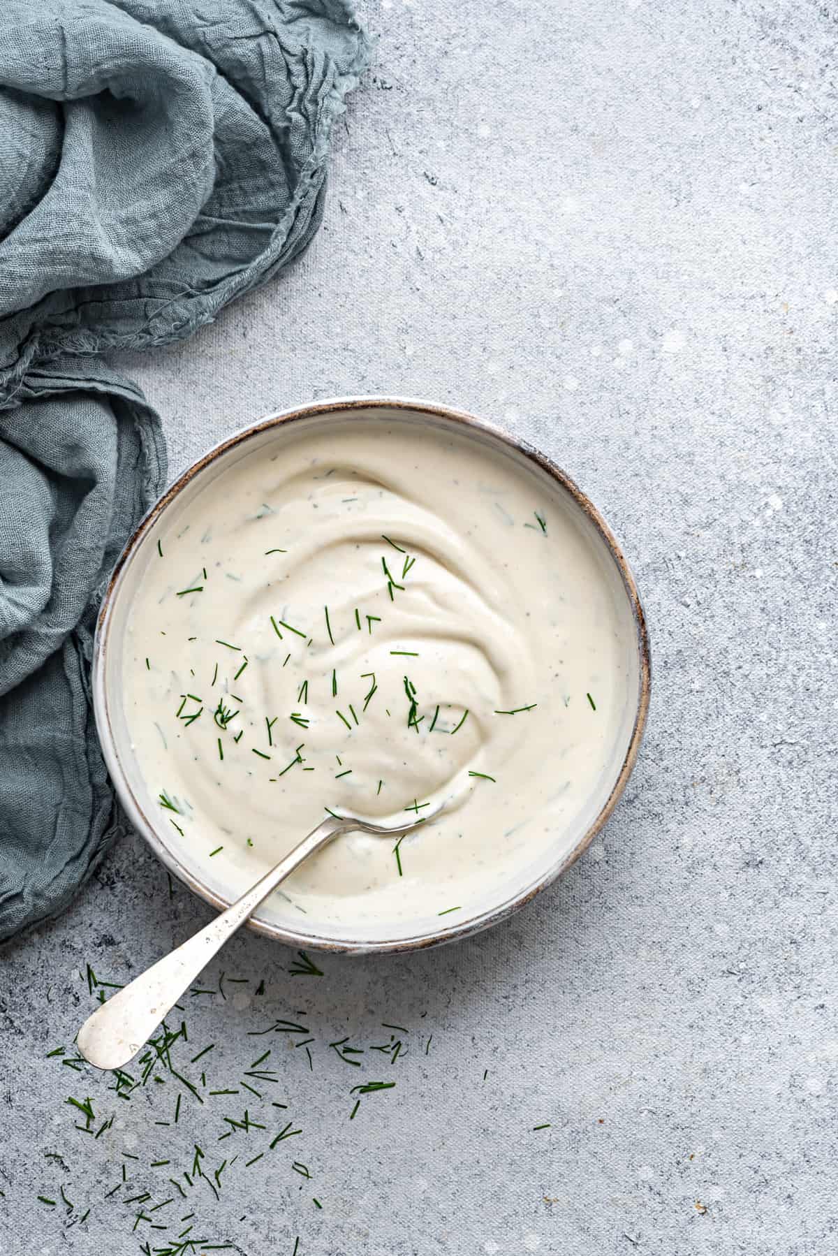 Top down view of a white earthen bowl with creamy dill sauce and a spoon into it.