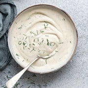 Top down close view of creamy lemon dill sauce in a white bowl with a silver spoon.