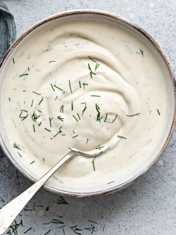 Top down close view of creamy lemon dill sauce in a white bowl with a silver spoon.