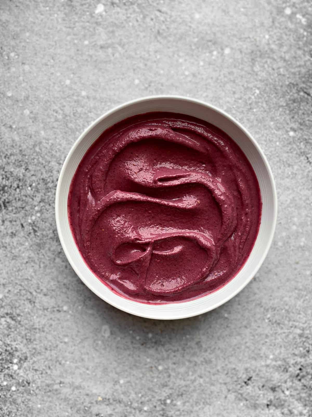 berry acai smoothie poured into a white bowl, spread across evenly.