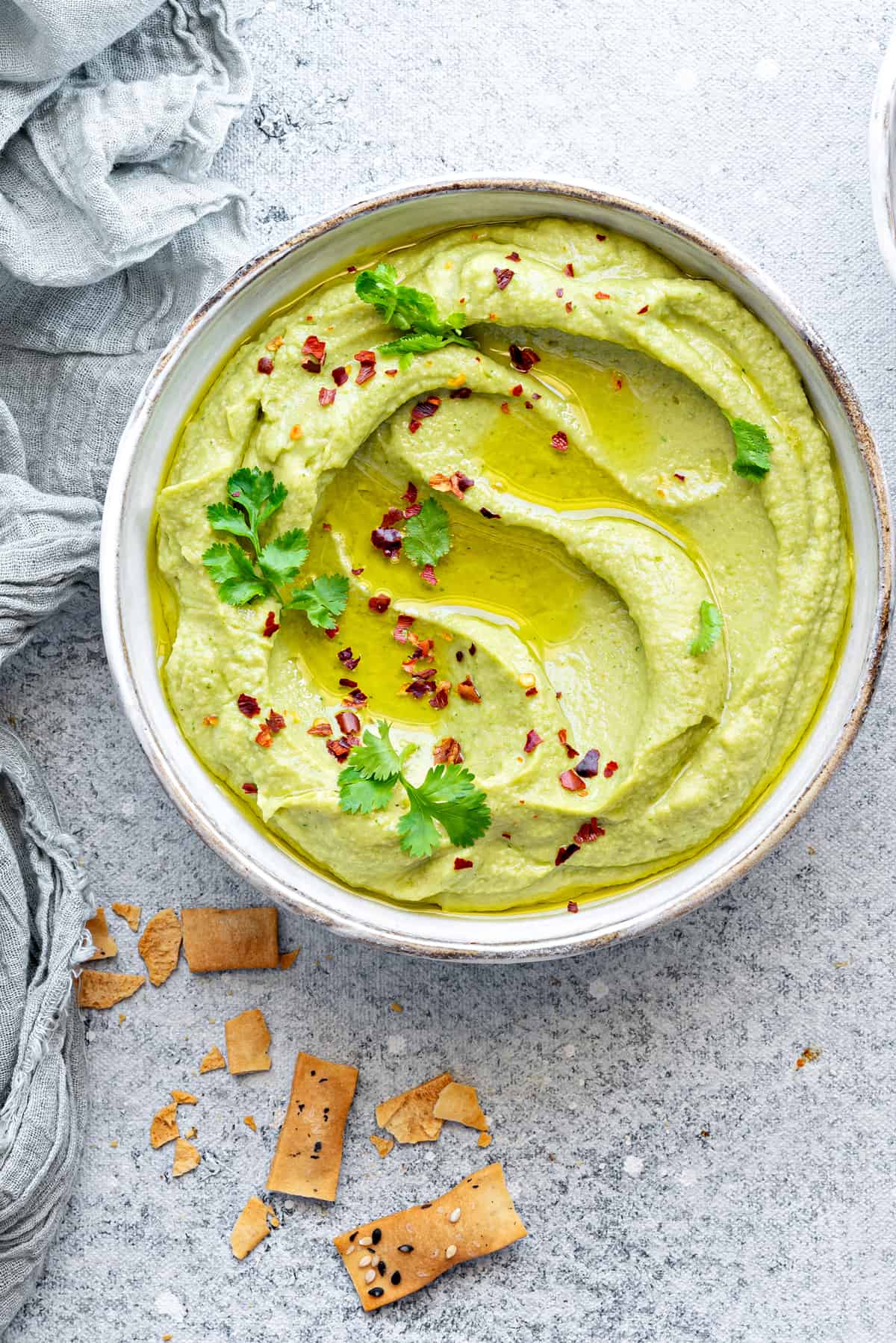 Close-up view of creamy avocado hummus in bowl, topped with fresh cilantro and red pepper flakes.