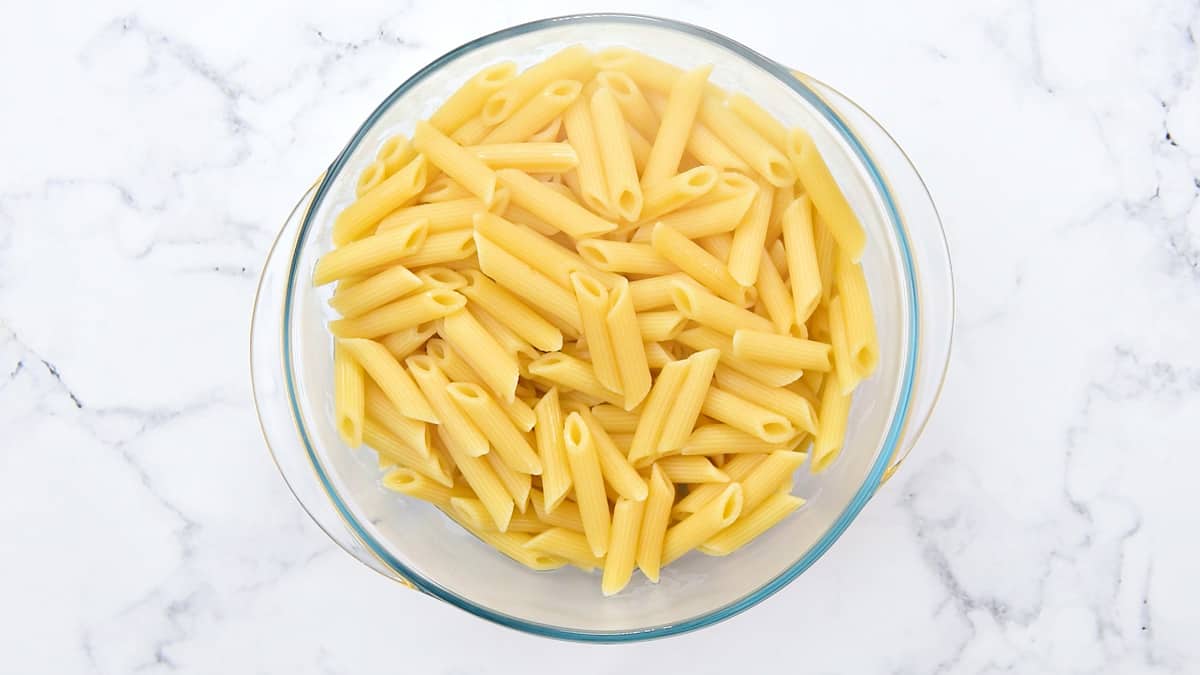 Cooked and drained penne noodles in a glass bowl.