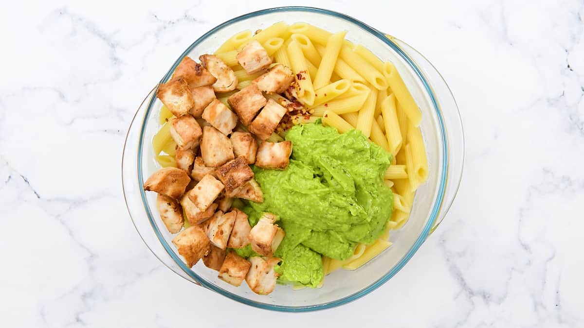 Chunks of chicken, noodles, and avocado sauce in a glass bowl.