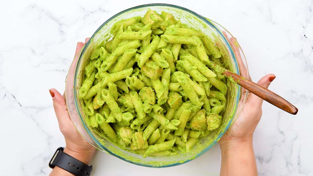 pasta, chicken and sauce combined in glass bowl, hands holding the bowl.