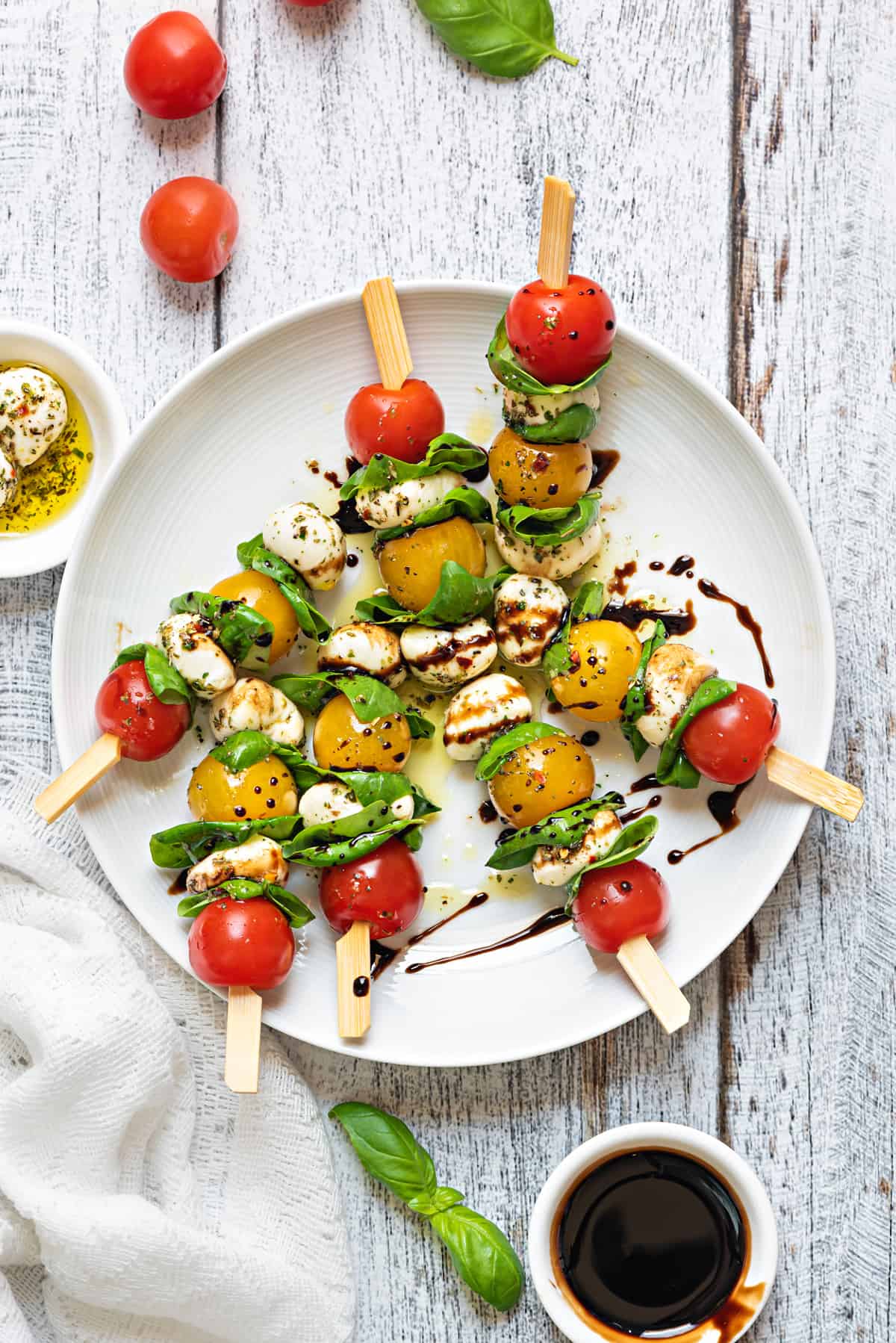 White plate with caprese skewers, all drizzled with balsamic glaze.