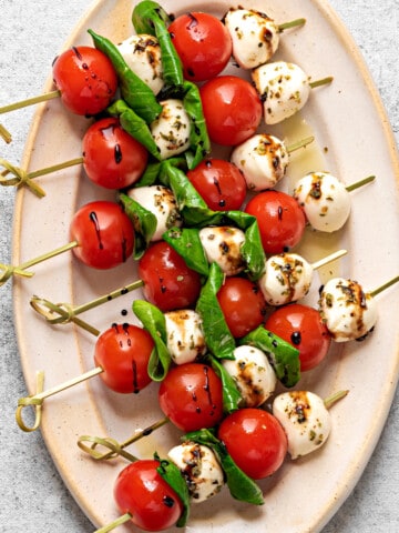 Large oval plate with 6 Caprese skewers drizzled with balsamic reduction.