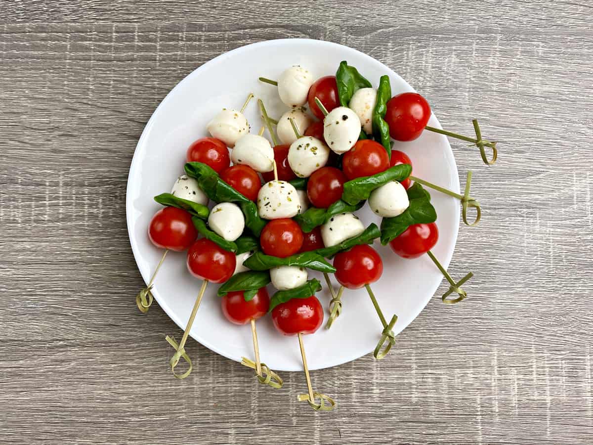 White round plate loaded with 8 Caprese skewers.