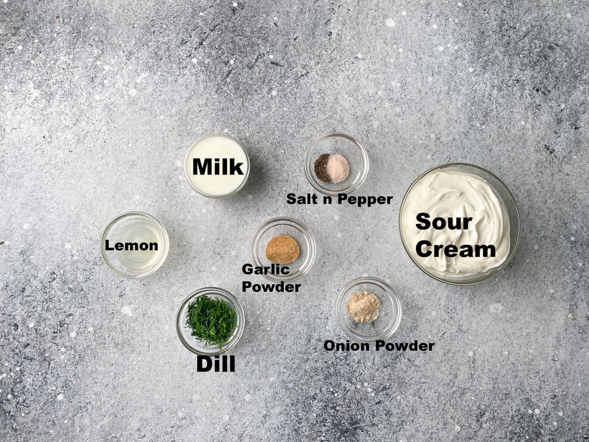 Recipe ingredients placed in individual glass bowls: sour cream, fresh dill, lemon juice, milk, onion and garlic powder, salt and pepper.