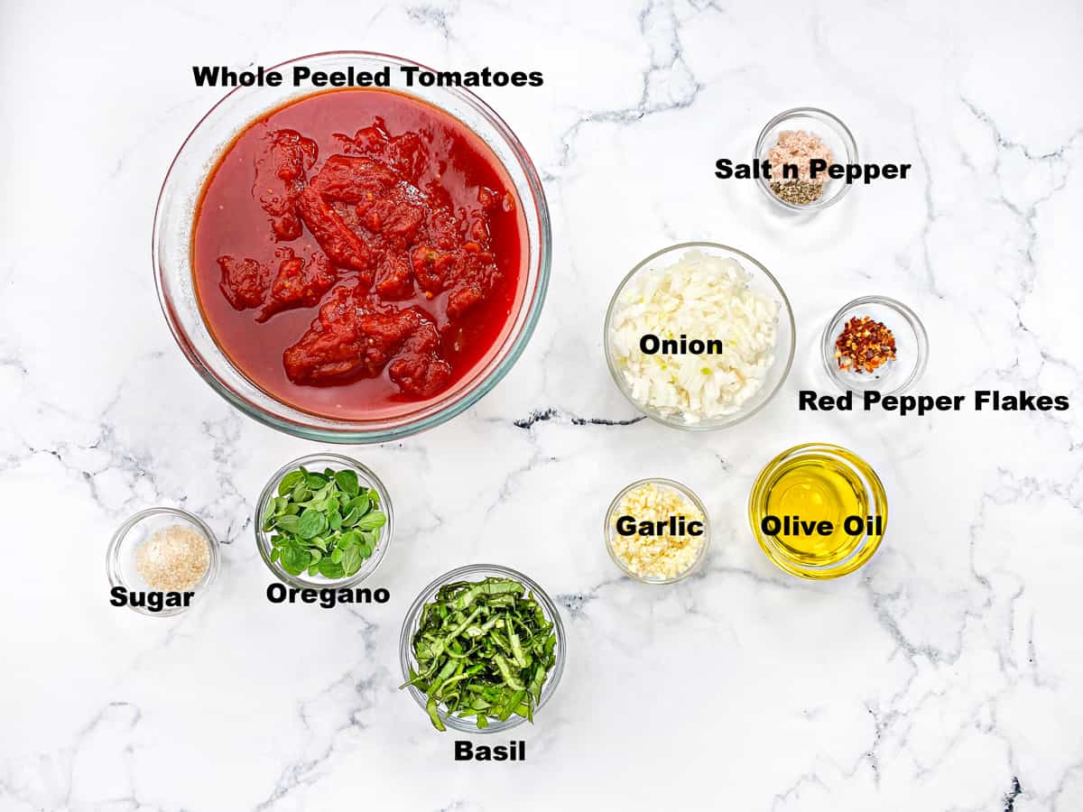 Top down view of recipe ingredients: peeled tomatoes, oil, garlic onion, herbs and seasonings in individual glass bowls. 