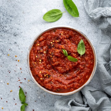 Bowl of homemade marinara sauce on a gray background. Little baby basil leaves scattered around.