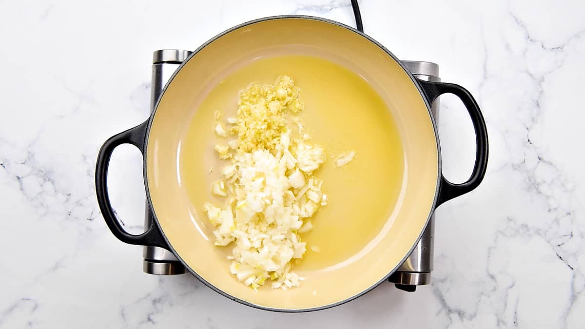 Minced garlic and onion added to the olive oil in a pot.