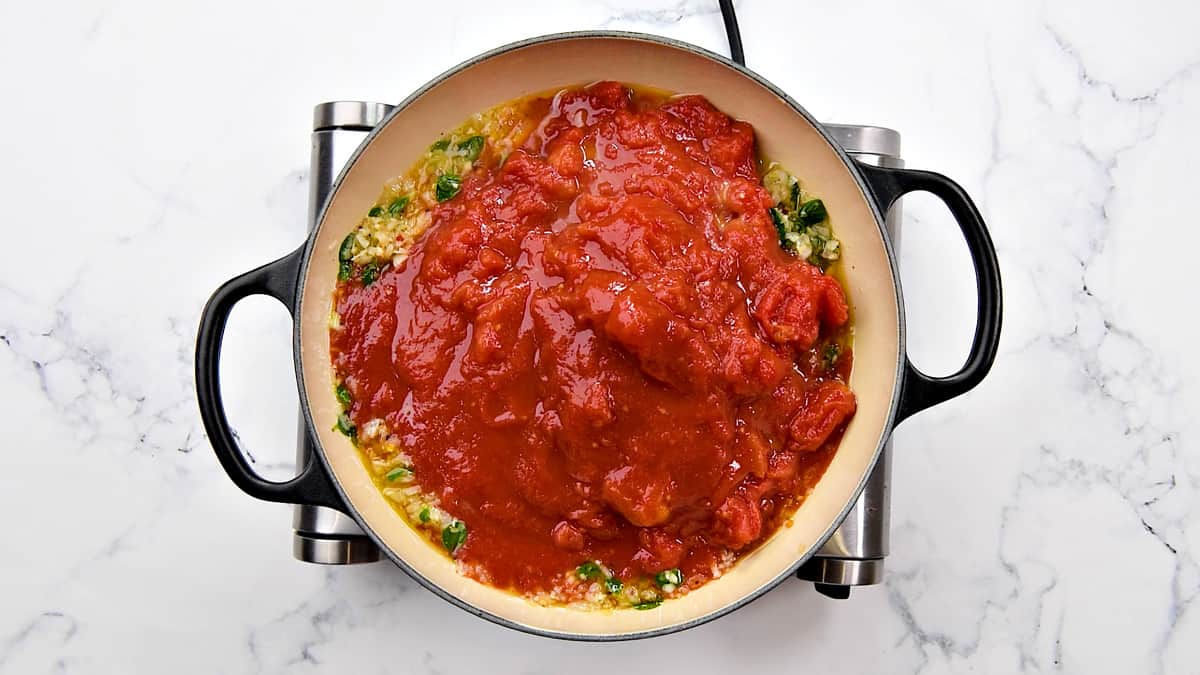 Adding canned crushed tomatoes to the pot.