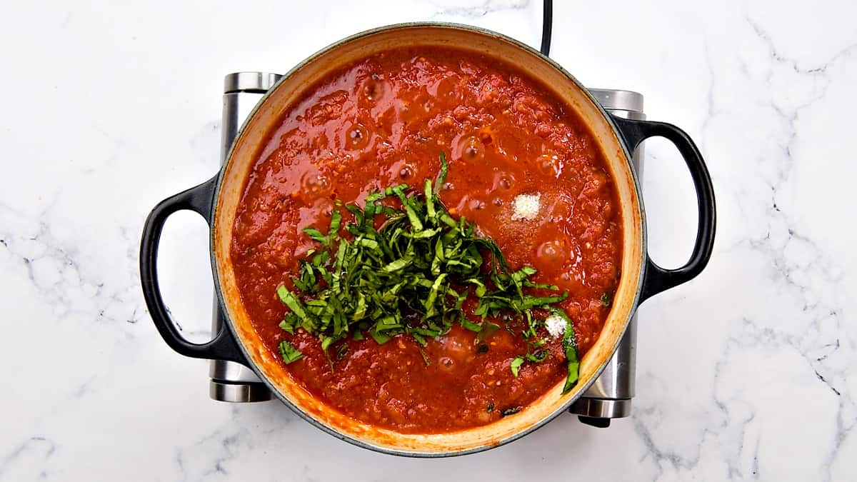 Fresh basil herb and sugar added to the tomato sauce in cooking pot.