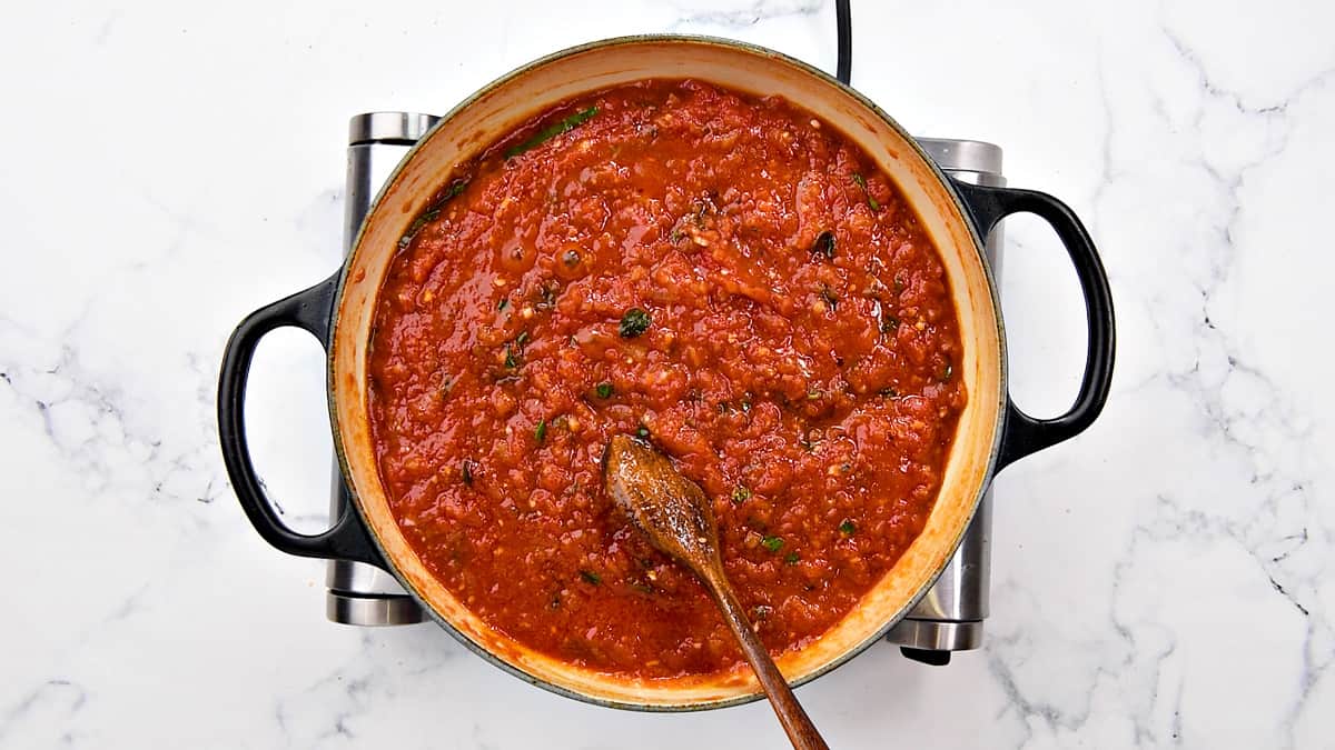 Homemade marinara sauce simmering in a large cooking pot, stirred with a wooden spoon.