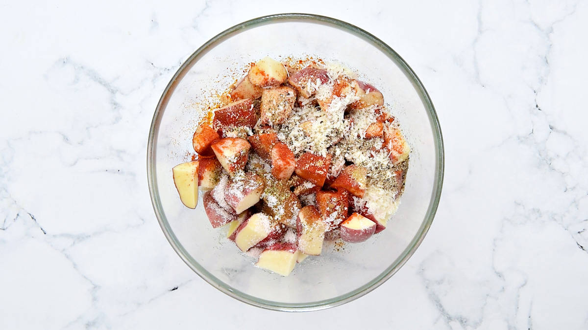 Shredded parmesan cheese on top of cubes red potatoes in a glass bowl.