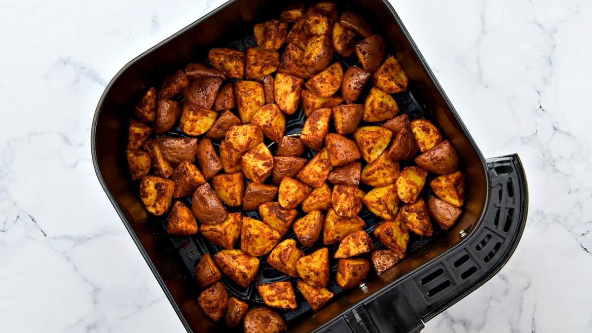 Seasoned Mexican potato cubes in an air fryer basket.